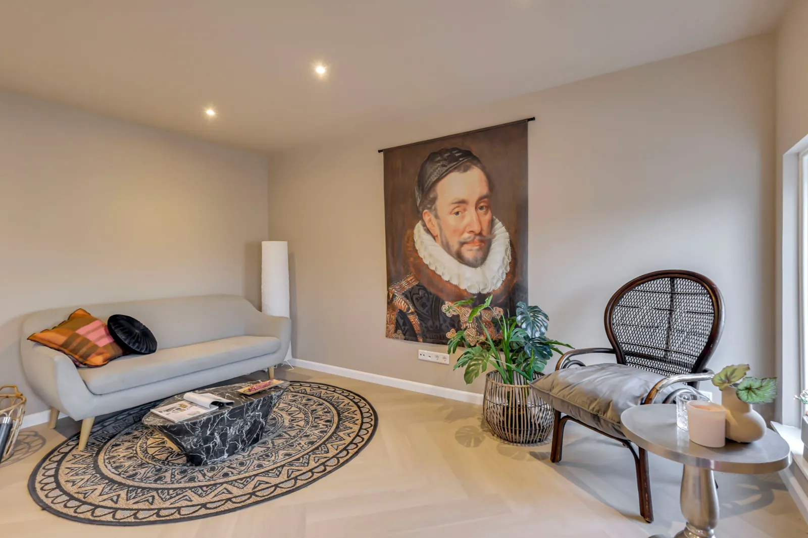 Woonkamer met visgraatvloer, lichtgrijze bank en een groot wandportret van Willem van Oranje